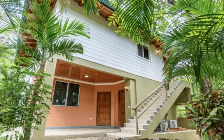 Cozy two-story tropical house surrounded by palm trees and greenery.