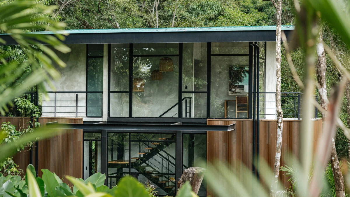 Modern two-story Costa Rica treehouse villa with black steel, glass walls, and natural wood, integrated into dense Manuel Antonio jungle.